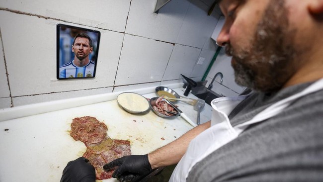 Chef Damian Zanotti, who works at the restaurant El Antojo, prepares a schnitzel, known as milanesa in Argentina, with the face of Argentina's soccer legend Lionel Messi, a day after he announced his retirement from the national team, in Buenos Aires
