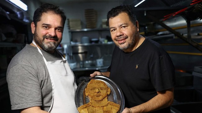 Chef Damian Zanotti and the owner of the restaurant El Antojo, Christian Franco, pose with a tray with a schnitzel, known as milanesa in Argentina, with the face of Argentina's soccer legend Lionel Messi, a day after he announced his retirement from