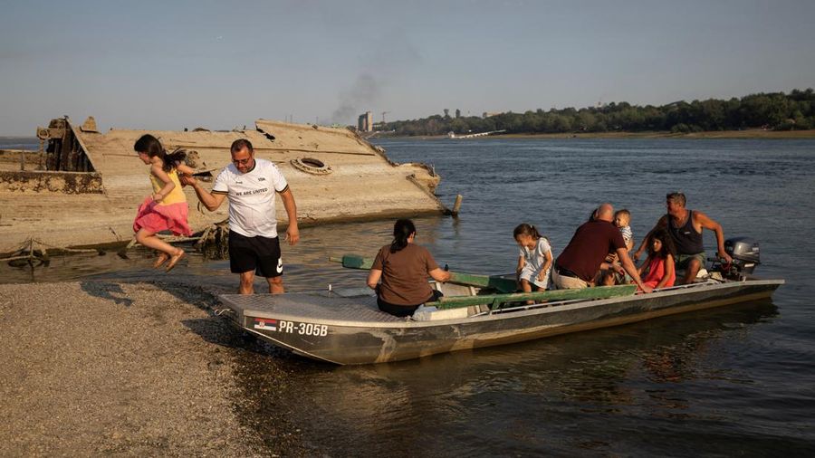 Seorang gadis melompat saat orang-orang turun dari perahu menuju gosong pasir di samping buntang kapal perang Jerman dari Perang Dunia II—yang muncul ke permukaan akibat surutnya air Sungai Danube lantaran kekeringan dan suhu panas ekstrem—di dekat Prahovo, Serbia, pada 13 Agustus 2026.