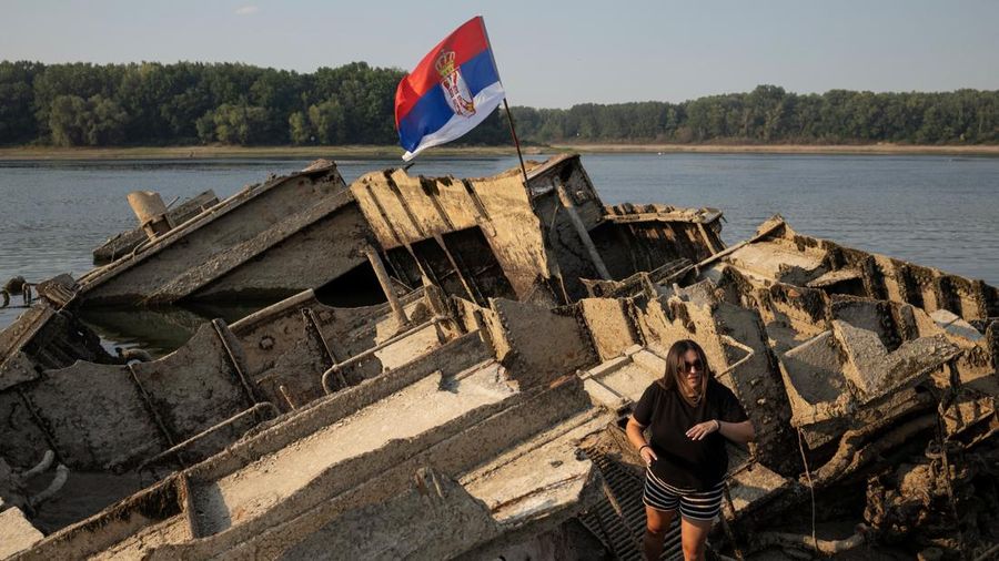 Seorang wanita berdiri di atas kapal perang Jerman dari Perang Dunia II nan tenggelam dan sekarang muncul ke permukaan akibat surutnya air Sungai Donau—yang disebabkan oleh kekeringan dan suhu panas ekstrem—di dekat Prahovo, Serbia, pada 13 Agustus 2026.