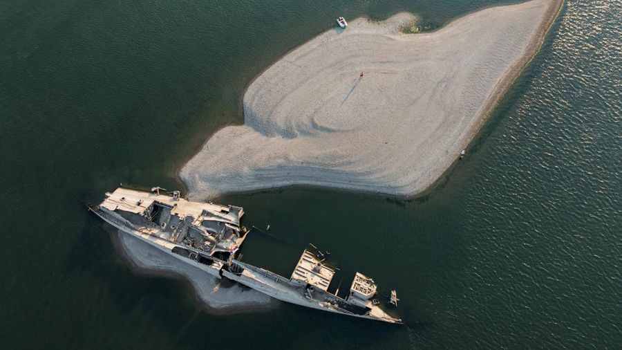 Tampilan dari drone nan memperlihatkan seorang laki-laki berdiri di dekat buntang kapal perang Jerman dari Perang Dunia II nan muncul ke permukaan akibat surutnya air Sungai Danube—yang disebabkan oleh kekeringan dan suhu panas ekstrem—di dekat Prahovo, Serbia, pada 13 Agustus 2026.