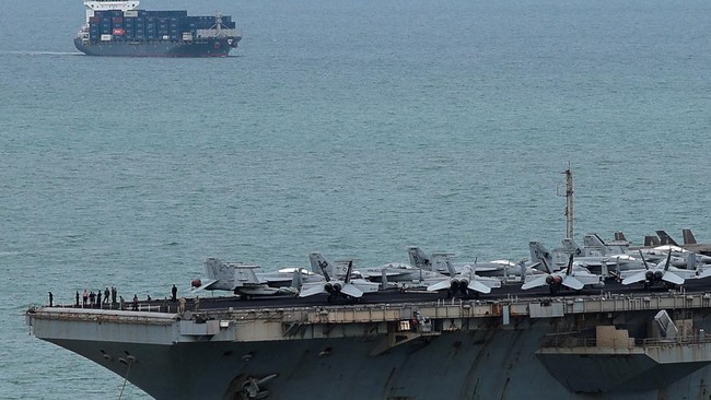 A container ship sails near the U.S. Navy Nimitz-class aircraft carrier USS Abraham Lincoln as the carrier heads toward Laem Chabang Port to dock for a rest stop following a long deployment in the Middle East, in Chonburi province, Thailand, Septembe
