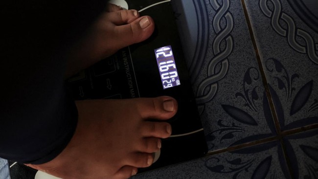 Intan Permatasari, 14, weighs herself on a digital scale at her home in Bogor, West Java province, Indonesia, May 13, 2026. Afraid of being seen in public, Intan would check no one was around before daring to go outside. At home, she would watch TV o