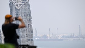 A man takes pictures of the haze hovering over the Singapore Strait waterway in Singapore on August 20, 2026. (Photo by Roslan RAHMAN / AFP)
