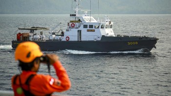A police boat is seen as a team member uses binoculars during search operations for a speedboat carrying eight people including five journalists, which went missing September 7 in waters of the Sunda Strait, on September 12, 2026. The five Indonesian