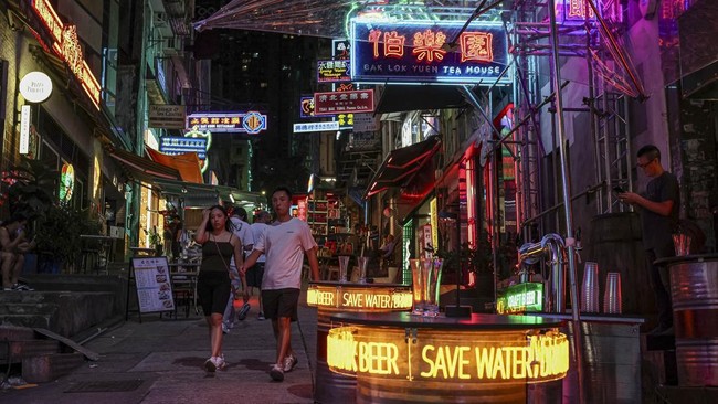 People walk along a street in Hong Kong's Soho district, decorated with temporary neon lights and market stalls for a film production, China, August 13, 2026. REUTERS/Tyrone Siu