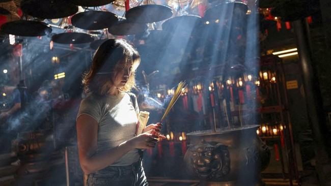A woman holding incense walks through Man Mo Temple in Hong Kong, China, July 24, 2026. REUTERS/Tyrone Siu     TPX IMAGES OF THE DAY