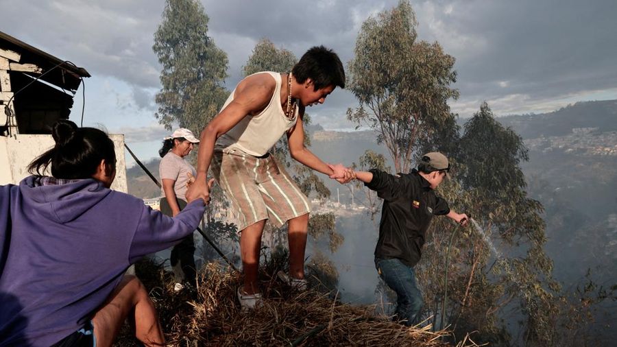 Kebakaran rimba di dekat area permukiman, sementara orang-orang bermain sepak bola di sebuah lapangan di Quito, Ekuador, Minggu (13/9/2026). (REUTERS/Karen Toro)