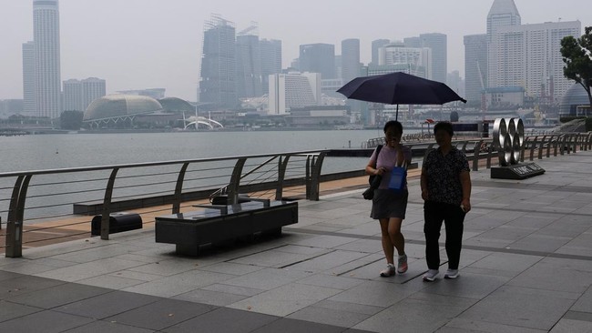 People walk along the bayfront with the city skyline shrouded in haze as smoke from regional forest fires reduces visibility across the island city-state, in Singapore, September 14, 2026. REUTERS/Suhaimi Abdullah