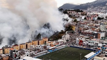 A drone view shows smoke rising from a hillside during a wildfire near residential neighbourhoods while people play soccer on a field in Quito, Ecuador, September 13, 2026. REUTERS/Karen Toro     TPX IMAGES OF THE DAY
