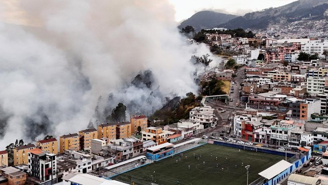 A drone view shows smoke rising from a hillside during a wildfire near residential neighbourhoods while people play soccer on a field in Quito, Ecuador, September 13, 2026. REUTERS/Karen Toro     TPX IMAGES OF THE DAY