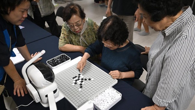 This picture taken on August 13, 2026 shows elderly people playing a game of Gomoku, also called five in a row, with a robot during a government-organised digital survival training at a senior community centre in Suwon. Age gaps in digital literacy a
