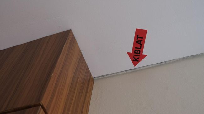 Qibla direction sign for Muslim prayer at the wall inside hotel room. Kiblat means qibla in English