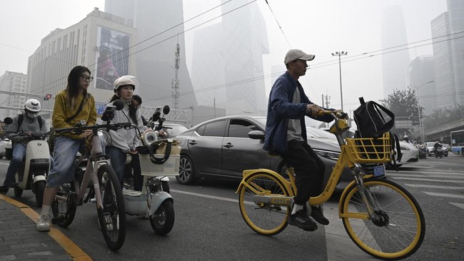 People wait to cross a road on a polluted day in Beijing on September 17, 2026. (Photo by GREG BAKER / AFP)