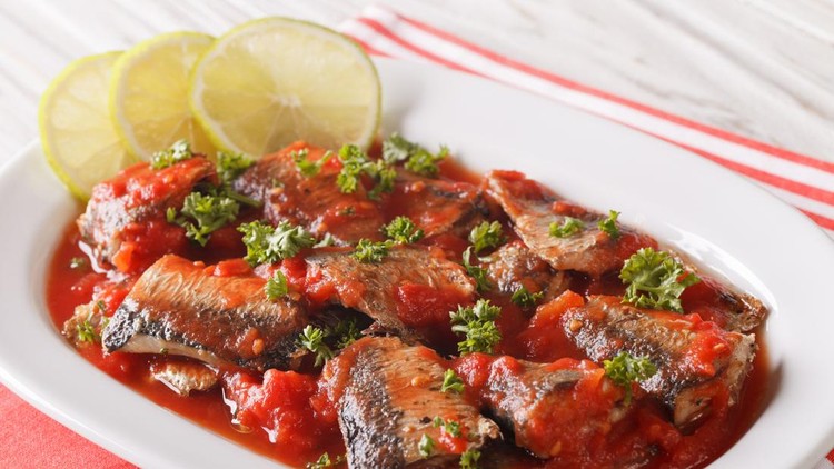 Braised sardines in tomato sauce with lime and parsley close-up on a plate&period; horizontal