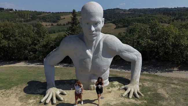 A drone view shows visitors walking past one of the giant human figures from the