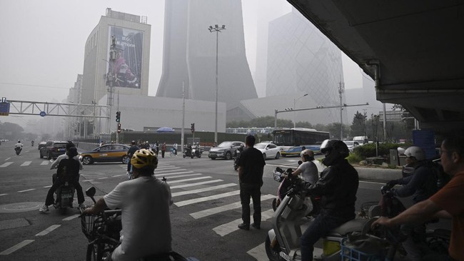 People wait to cross a road on a polluted day in Beijing on September 17, 2026. (Photo by GREG BAKER / AFP)
