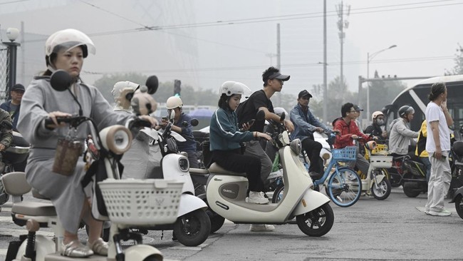 People ride on scooters and bicycles on a polluted day in Beijing on September 17, 2026 (Photo by GREG BAKER / AFP)