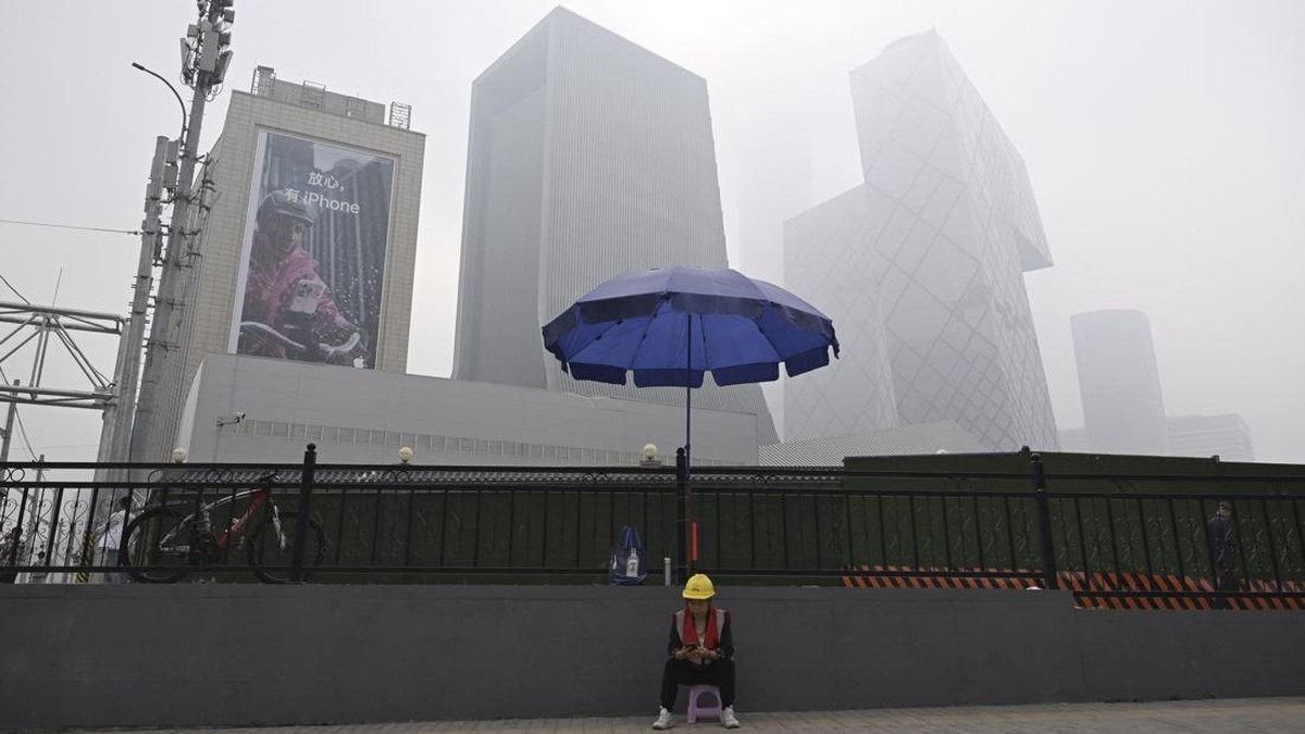 A woman sits under an umbrella on a polluted day in Beijing on September 17, 2026. (Photo by GREG BAKER / AFP)