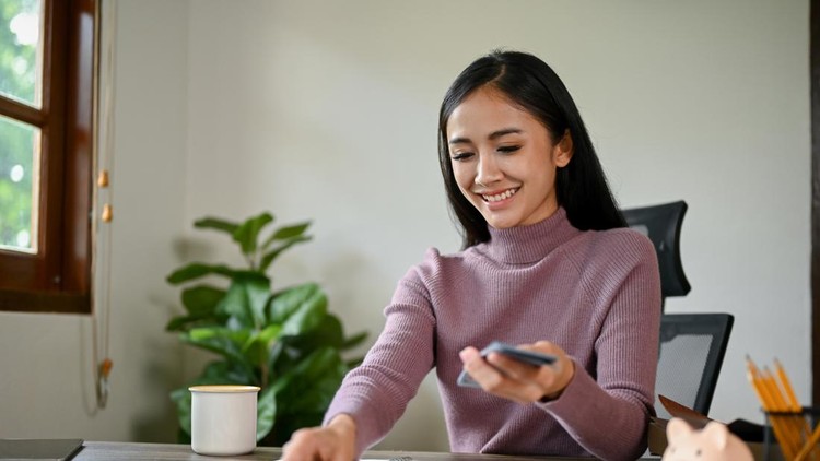 An attractive and happy Asian female counting her money at a table&comma; planning her savings and managing her monthly household expenses&period;