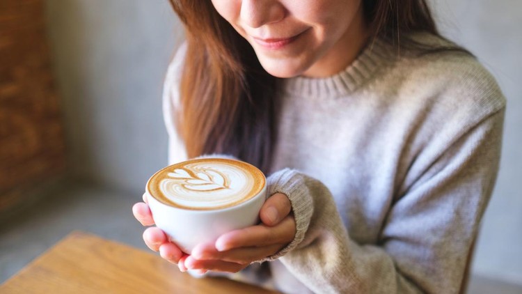 Closeup image of a woman holding a cup of hot latte coffee