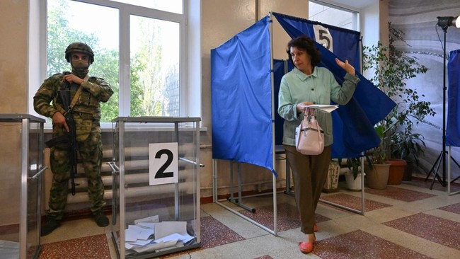 A woman leaves a voting booth to cast her ballot for Russia's parliamentary election as a Russian serviceman secures a polling station in Donetsk, Russian-controlled Ukraine, on September 18, 2026, amid the ongoing Russian-Ukrainian conflict. (Photo 