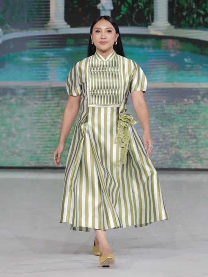 Tak kalah menarik, dibawakan oleh Afifah Yusuf, koleksi ini memiliki tampilan yang simple dan soft dengan warna hijau-putihnya. Bagian dada memiliki motif garis vertikal yang lebih rapat, lengan dress dibuat sedikit mengembang, dan rok melebar dengan panjang midi. Koleksi ini menampilkan kesan feminin dan playful dengan aksen pita di pinggang.&nbsp;(Foto: Dok. Senayan City)