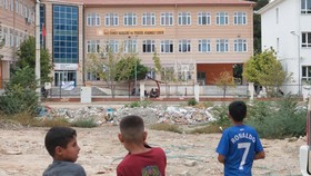 Children look at a high school where a gunman opened fire wounding eleven people and was detained shortly afterwards, in Turgutlu, an area west of the resort city of Izmir, on September 22, 2026. A teenager opened fire outside a high school in wester