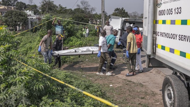 South African forensic pathology personnel are assisted by community members to load the bodies of victims into a mortuary van following a mass shooting in the Ziko area of KwaMakhutha, south of Durban on September 23, 2026. Armed men stormed a home