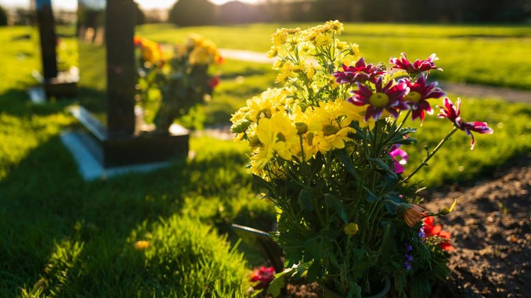 Dusk at a winter's English cemetery seen with in-focus flowers in a burial plot&period; A number of fresh marble headstones can be seen&period;