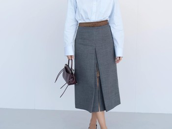 Camila Mendes memadukan midi skirt abu-abunya dengan kemeja biru muda. Detail yang quirky, seperti kerah pita ganda dan lapisan rok beda warna jadi daya tarik penampilannya./ Foto: Courtesy of Prada