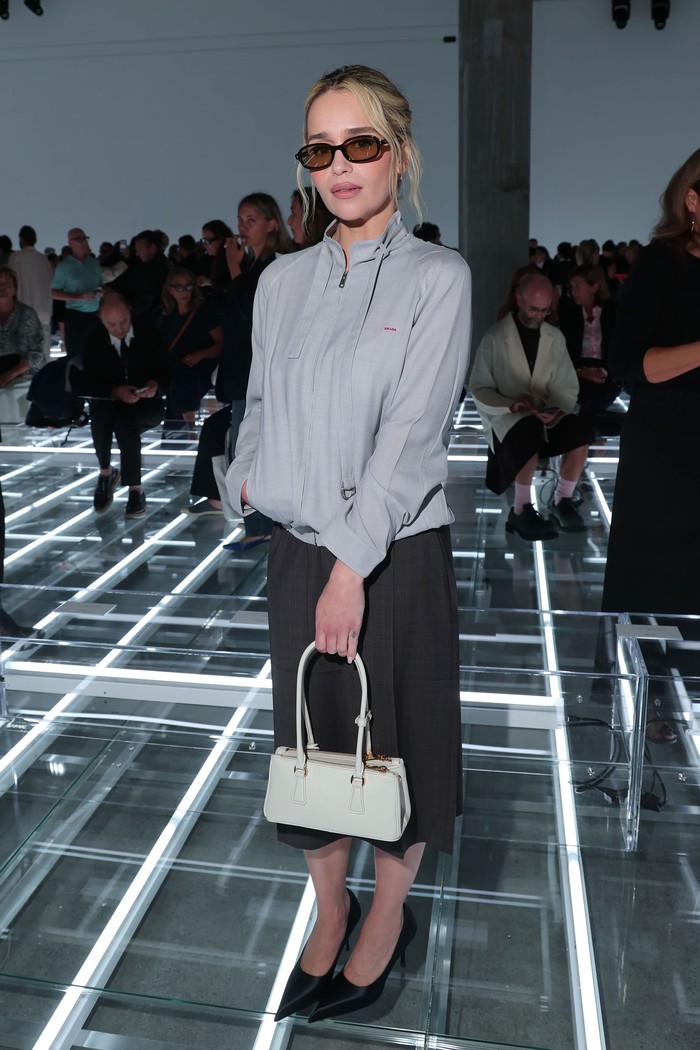 Gaya yang santai dan sporty diadopsi Emilia Clarke. Aktris asal Inggris itu mengenakan rok selutut dan jaket dengan aksen tali dalam warna abu-abu yang serasi. Mempermanis tampilan, ia menggenggam shoulder bag berstruktur rona putih, sedangkan sunglasses sebagai sentuhan vintage/ Foto: Courtesy of Prada