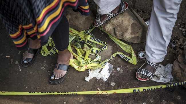 Residents stand behind police tape near the scene where gunmen armed with assault rifles stormed a bar in Johannesburg on September 27, 2026. Gunmen killed at least 27 people in two mass shootings in South Africa's two main cities, police said on Sep