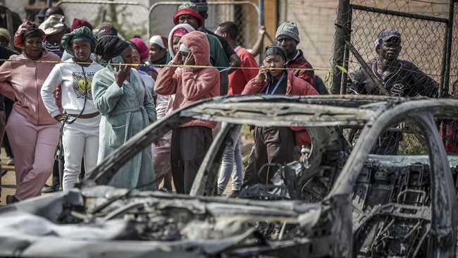 Residents stand behind police tape near the scene where gunmen armed with assault rifles stormed a bar in Johannesburg on September 27, 2026. Gunmen killed at least 27 people in two mass shootings in South Africa's two main cities, police said on Sep