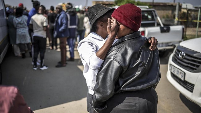 A resident comforts another person near the scene where gunmen armed with assault rifles stormed a bar in Johannesburg on September 27, 2026. Gunmen killed at least 27 people in two mass shootings in South Africa's two main cities, police said on Sep