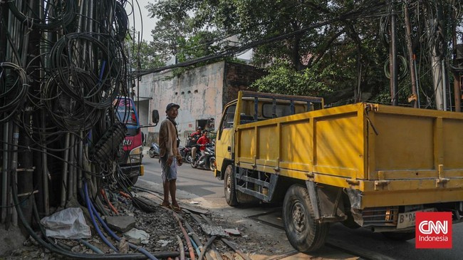Sejumlah kabel optik tampak semrawut dan menjuntai di sepanjang area trotoar di kawasan Jalan Kuningan Barat, Jakarta, Senin, 28 September 2026. Kabel-kabel tersebut terlihat melintang di antara pepohonan sekitar jalan. CNN Indonesia/Febria Adha L