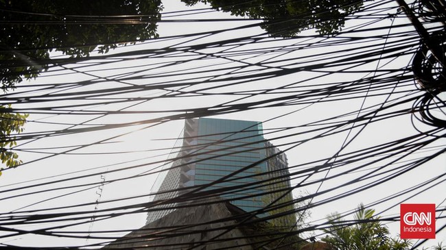 Sejumlah kabel optik tampak semrawut dan menjuntai di sepanjang area trotoar di kawasan Jalan Kuningan Barat, Jakarta, Senin, 28 September 2026. Kabel-kabel tersebut terlihat melintang di antara pepohonan sekitar jalan. CNN Indonesia/Febria Adha L