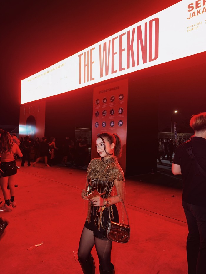 Diva Azzura tampil stylish saat menonton konser The Weeknd di Jakarta. Ia mengenakan atasan gold berhias fringe, mini shorts hitam, sheer tights, dan knee-high boots yang menciptakan kesan glamor dan edgy/Foto: Instagram/diva.azzura