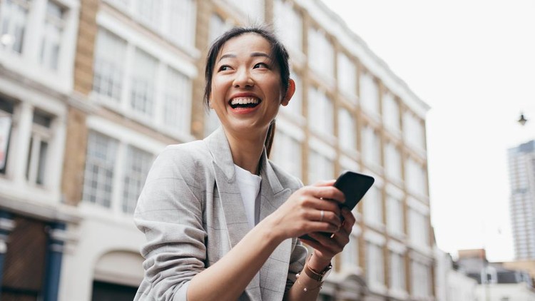 Asian business woman looking far away while using her smartphone on the street of London&period;