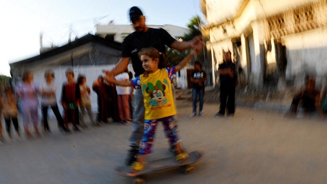 A Palestinian girl skateboards as skateboarder, displaced coach and Gaza Skate Team leader Rajab Al-Rifi instructs her, in Gaza City, September 23, 2026. REUTERS/Mahmoud Issa