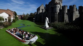 A sightseeing boat travels along a duckweed-covered section of the River Lys in front of the Gravensteen castle in Ghent, Belgium, October 5, 2026. Prolonged hot and dry weather led to a surge in duckweed growth on the river following one of Europe's