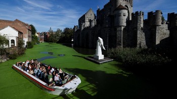 A sightseeing boat travels along a duckweed-covered section of the River Lys in front of the Gravensteen castle in Ghent, Belgium, October 5, 2026. Prolonged hot and dry weather led to a surge in duckweed growth on the river following one of Europe's