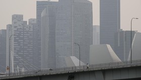 A pedestrian walks along a bridge as city skyline is seen shrouded with haze in Singapore on October 8, 2026. Toxic haze has shrouded parts of Indonesia, Malaysia and Singapore for weeks as Jakarta struggles to contain fires that have scorched large