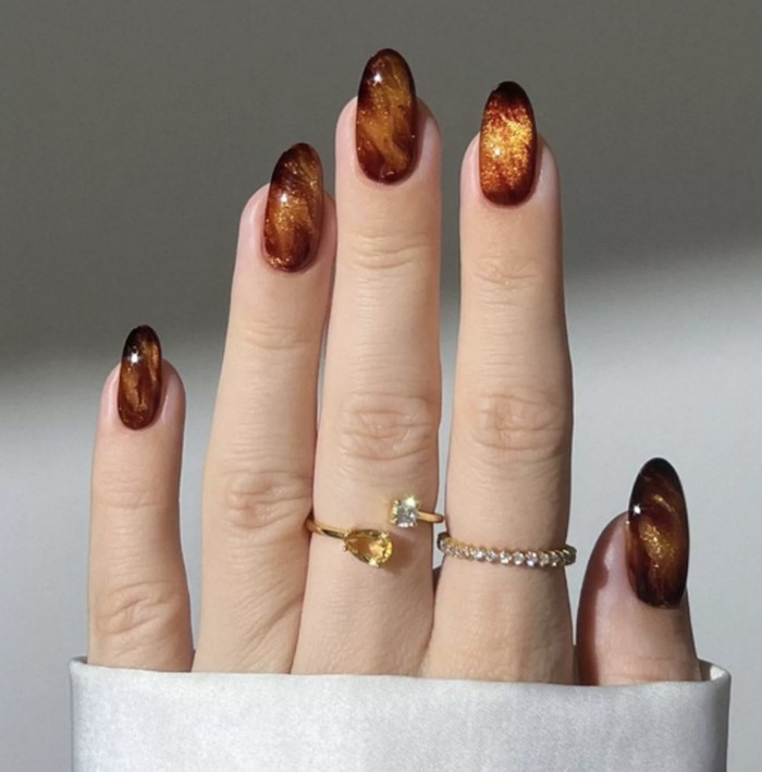 Pumpkin spice syrup nails menghadirkan warna amber dengan kilau yang menyerupai sirup rempah. Desain ini cocok untuk pecinta manikur berkilau dengan sentuhan hangat dan elegan. Foto: instagram.com/heygreatnails