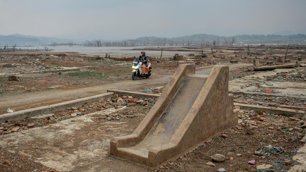 Pengendara roda dua melintas di samping taman bermain yang muncul kembalu di tepian Waduk Jatigede yang surut di Desa Cipaku, Kecamatan Darmaraja, Kabupaten Sumedang, Jawa Barat, Minggu (11/10/2026). Berdasarkan data dari Badan Penanggulangan Bencana