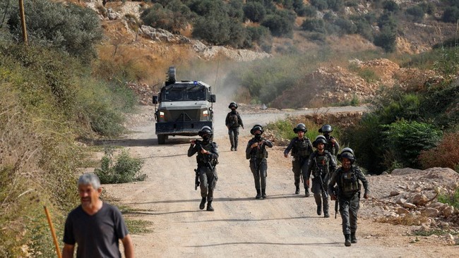 A Palestinian man walks near Israeli soldiers as Palestinians farmers, who pick olives during the harvest season, react during clashes with Israeli settlers in Palestinian-owned olive groves in the village of Deir Abu Mishal, near Ramallah, in the Is