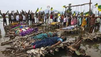 Protesters and members of families affected by the Ken-Betwa River Link Project lie on symbolic funeral pyres placed in the water, while others stand beneath a wooden frame with symbolic nooses around their necks during a protest near the Majhgawan D