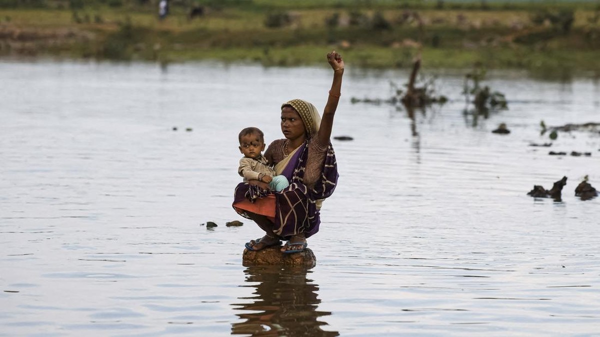 Savita Devi, a member of a family affected by the Ken-Betwa River Linking Project, holds her child while sitting on a stone and raises her fist as she shouts slogans demanding compensation and proper rehabilitation during a protest near the Majhgawan