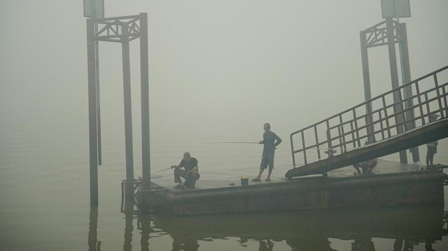 People fish on the Musi River as haze from wildfires shrouds the area in Palembang, South Sumatra province, Indonesia, October 15, 2026. REUTERS/Abriansyah Liberto