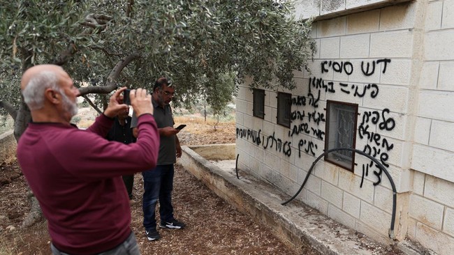 A man takes a picture of a graffiti sprayed on a wall of a mosque, reading